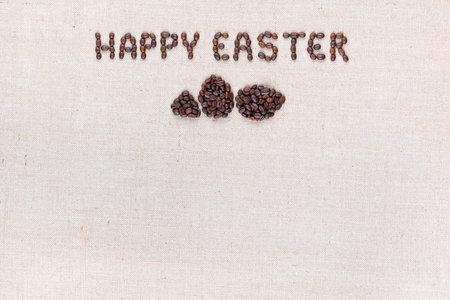 The words Happy easter above some small eggs all made with coffee beans on creamy linea canvas, shot from above, aligned at the top.の写真素材