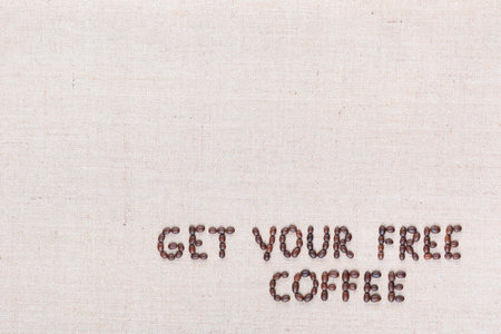 The message Get your free coffee written with coffee beans on creamy linea canvas, shot from above, aligned at the bottom right.の写真素材