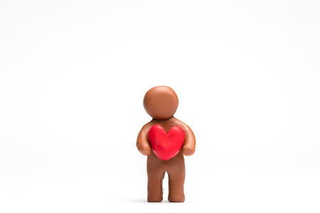 A man made from plasticine holding a heart on white background, aligned in the center.の写真素材