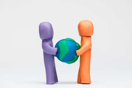 Two people made from plasticine of different colors pulling a model of planet earth away from one another.の写真素材