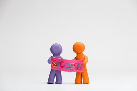 Two people made from plasticine holding a pink poster with the word success written on it, on white...