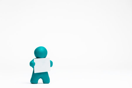A man made from plasticine holding a blank sheet of paper on white background, aligned to the left.の写真素材