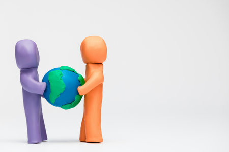 Two people made from plasticine of different colors pulling a model of planet earth away from one another.の写真素材
