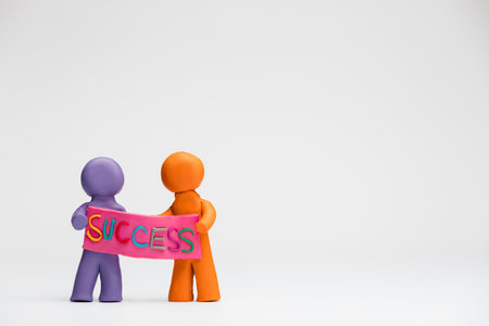 Two people made from plasticine holding a pink poster with the word success written on it, on white background, aligned to the left.の写真素材