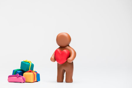 A man made from brown plasticine next to a big pile of gifts on white background , aligned in the center.の写真素材