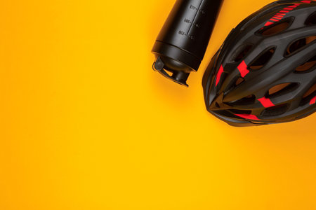 A black helmet next to a water bottle on yellow background , shot from above.