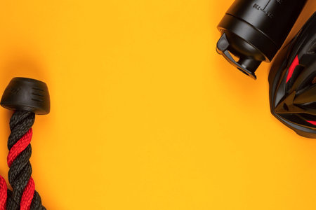 A black helmet next to a water bottle and rope on yellow background , shot from above.