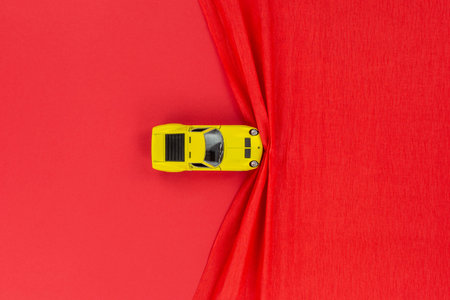 A yellow car figurine on a red wrinkled background, shot from above.の写真素材