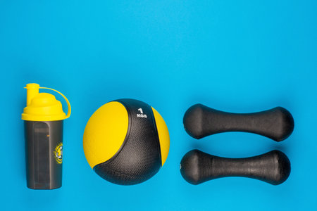 A pair of heavy dumbbells next to a ball and a water bottle on blue background, shot from above.の写真素材