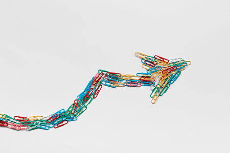 An arrow made from colored paperclips pointing upwards on a white background, shot from above.の写真素材