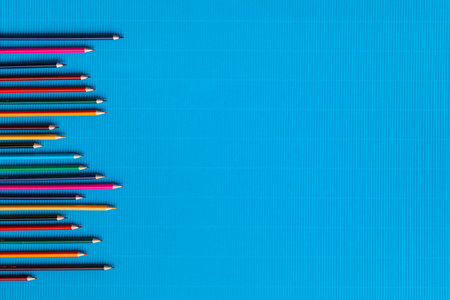A bunch of colorful crayons of different sizes arranged randomly on a blue background, shot from...