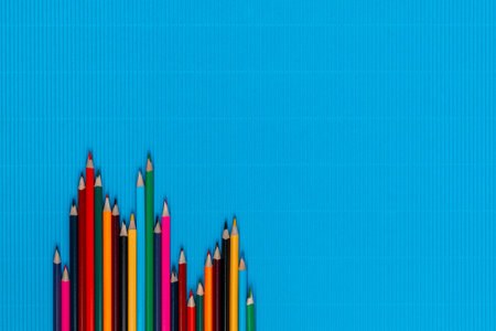 A bunch of colorful crayons of different sizes on a ocean blue background, shot from above, aligned at the bottom left, closeup.の写真素材