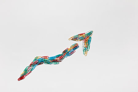 An arrow made from colored paperclips pointing upwards on a white background, shot from above.の写真素材