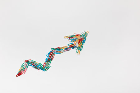 An arrow made from colored paperclips pointing upwards on a white background, shot from above.の写真素材