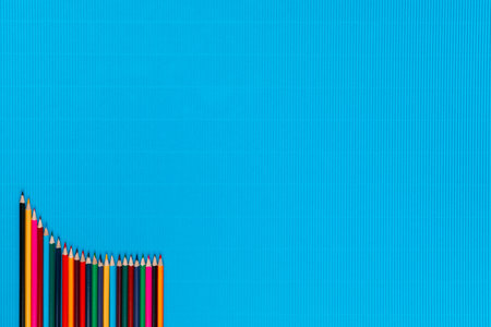 A bunch of colorful crayons arranged in a descending order on an ocean blue background, shot from above, aligned at the bottom left.の写真素材