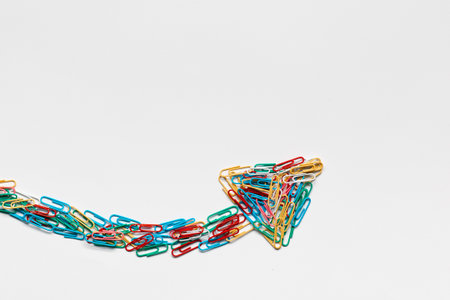 An arrow made from colored paperclips pointing upwards on a white background, shot from above.の写真素材