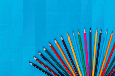 A bunch of colorful crayons arranged in a semi circle on an ocean blue background, shot from above, aligned at the bottom, closeup.の写真素材