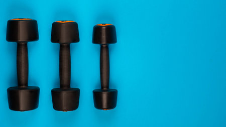 Two black dumbbells on blue background, shot from above.の写真素材