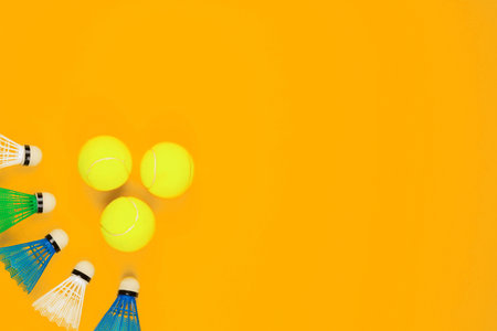 Three green tennis balls next to a bunch of colorful shuttlecocks, on yellow background, shot from above.の写真素材