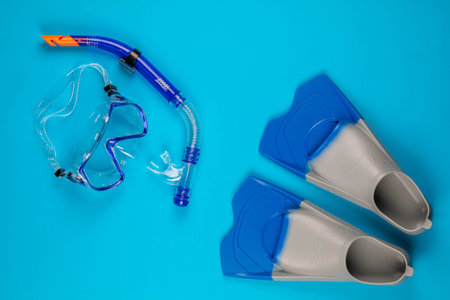 A pair of swimming goggles next to a pair of blue fins , on blue background, shot from above.の写真素材
