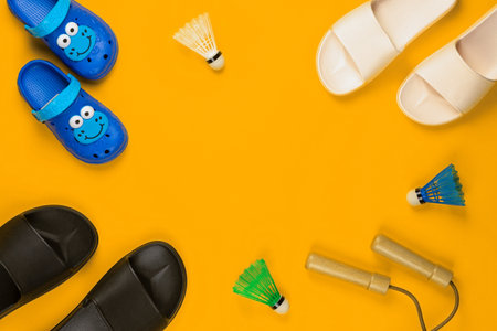 Gym equipment next to three pair of slippers on yellow background, shot from above, aligned at the bottom left.の写真素材