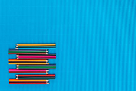 A bunch of colorful crayons of different sizes arranged randomly on a blue background , shot from above, arranged to the left.の写真素材