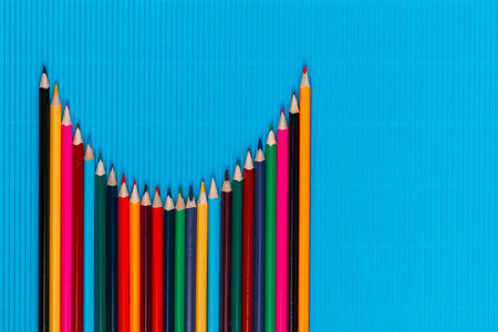 A bunch of colorful crayons arranged like a parabola on an ocean blue background, shot from above, aligned at the bottom left, closeup.の写真素材