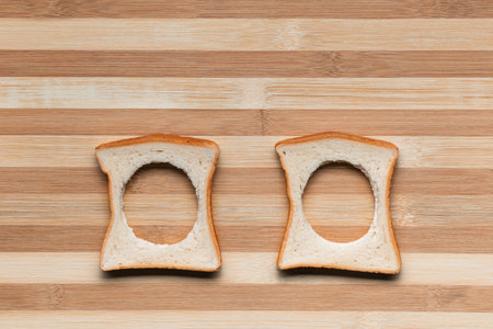 Two slices of bread with their centers cut on a brown table, shot from above.の写真素材