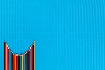 A bunch of colorful crayons arranged like a parabola on an ocean blue background, shot from above, aligned at the bottom left.の写真素材