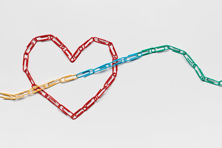 An arrow made from colored paperclips pointing upwards passing through a heart on a white background, shot from above, closeup.の写真素材