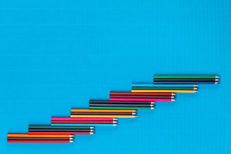 A bunch of colorful crayons spread diagonally on an ocean blue background , shot from above , arranged from the center to the bottom left.の写真素材