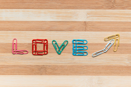 The word love next to an arrow pointing upwards all made from colorful paperclips on a table, shot from above, aligned in the center closeup..の写真素材