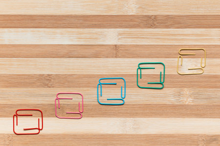 Colorful paperclips on a table, shot from above, arranged diagonally from bottom left towards the top right.の写真素材