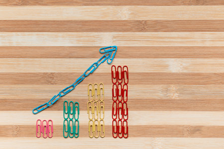 An arrow siting on a bunch of paperclips arranged in columns on a brown table, shot from above.の写真素材