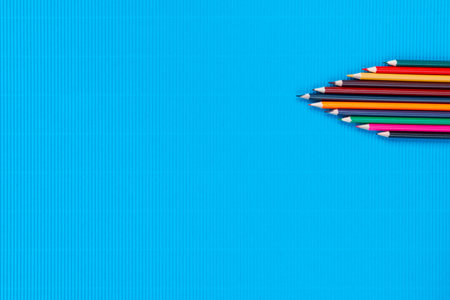 A bunch of colorful crayons of different sizes on a ocean blue background, shot from above , arranged at the top right.の写真素材