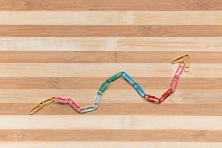 An arrow made from paperclips pointing upwards on a table, shot from above.の写真素材