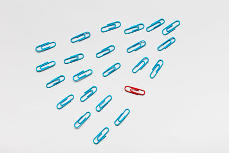 A bunch of blue paperclips aligned and one red paperclip nonaligned on white background , shot from above, closeup.の写真素材