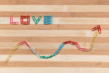 The word love next to an arrow pointing upwards all made from colorful paperclips on a table, shot from above.の写真素材