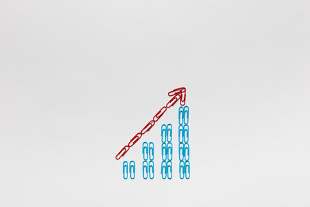 A red arrow pointing upwards siting on a stairwell made from blue paperclips on white background, shot from above.の写真素材