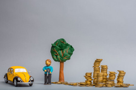 Plasticine man holding a key under a plasticine man in between a yellow car figurine and a big pile of golden coins, on gray background.の写真素材