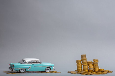 Light blue, retro car figurine next to an enormous pile of golden coins, on gray background.
