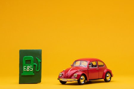Cool red car figurine aligned to the right next to a pale green sign representing a filling station, on orange background.の写真素材