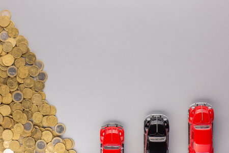 Top view of some car figurines placed next to a large heap of golden coins, on gray background.の写真素材