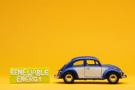 Cool blue car figurine aligned to the right next to a yellow sign with the words renewable energy on it, on orange background.の写真素材