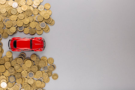 Top view of a red car figurine in between two big heaps of golden coins, on gray background.の写真素材