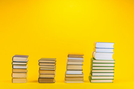 Columns of different sizes made from books on yellow background.の写真素材