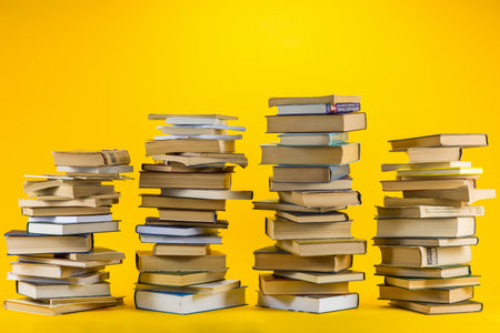 Four different sized columns made from books on yellow background.の写真素材