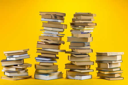 Four different sized columns made from books on yellow background.の写真素材