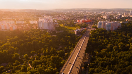 Aerial view of a highway road located in the middle of a green forest leading towards a big city, during a majestic sunrise.の写真素材