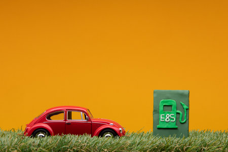 Chisinau, Moldova - August 15th 2019: A red car figurine aligned to the left on grass next to a pale green sign representing a filling station, on orange background.のeditorial素材